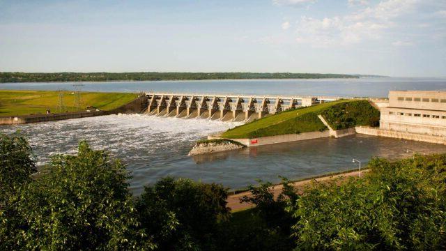 A dam with green landscape around it and a blue sky in the background